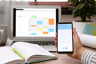 Photo of Woman holding smartphone with calendar app at table, closeup