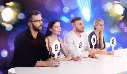 Image of Panel of judges holding different score signs at table against blurred background