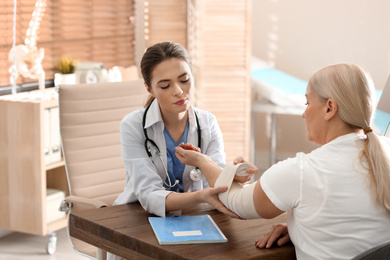 Photo of Female orthopedist applying bandage onto patient's elbow in clinic