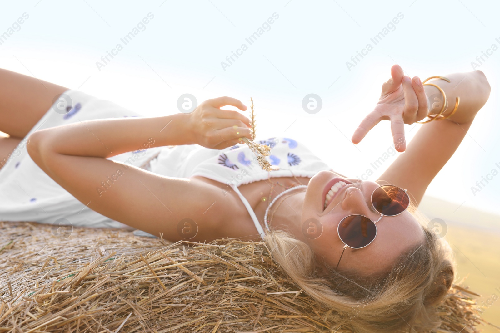 Photo of Beautiful hippie woman with spikelets showing peace sign on hay bale in field