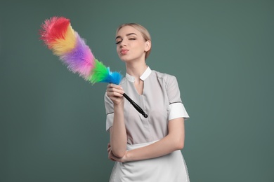 Photo of Young chambermaid with dusting brush on color background