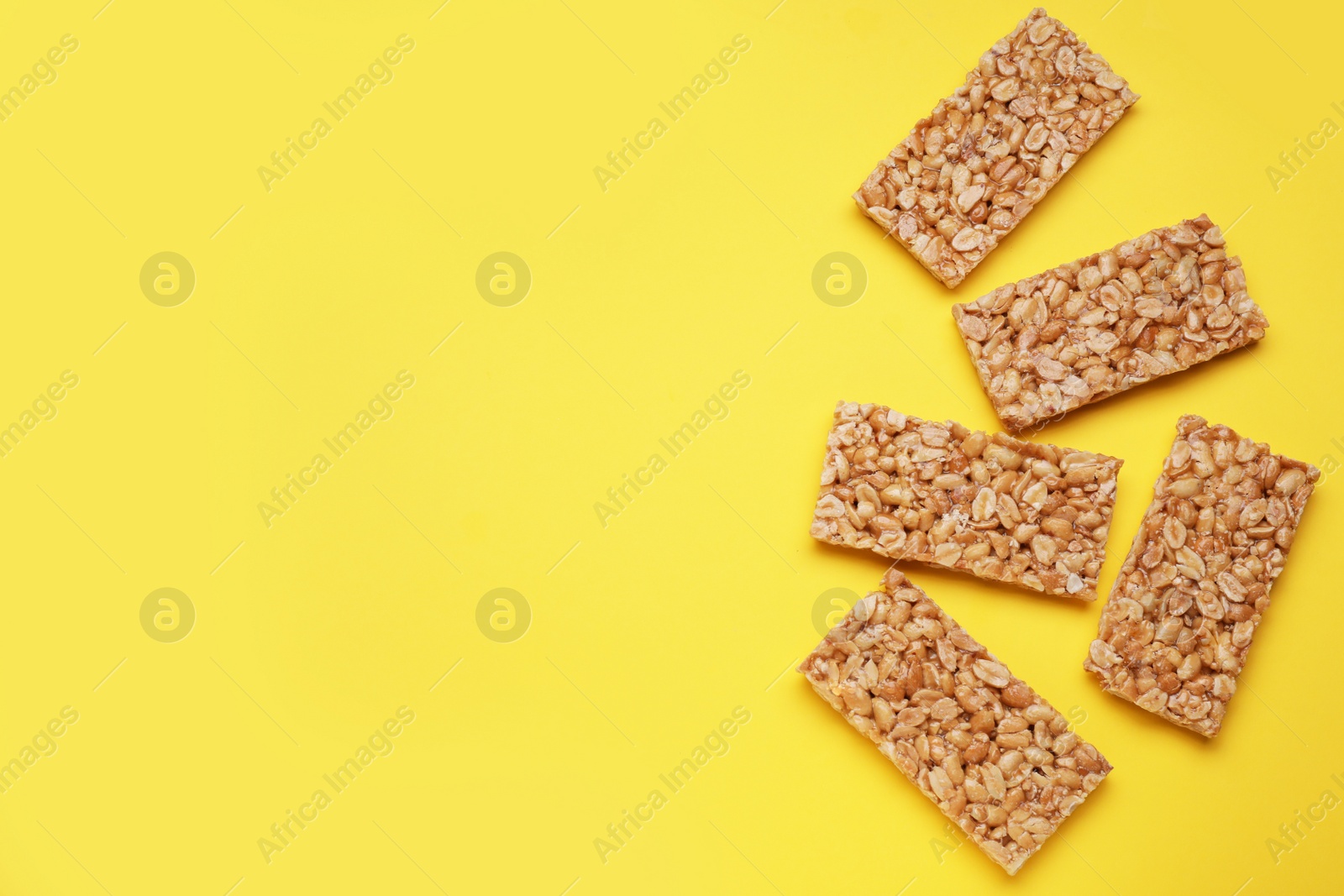 Photo of Tasty peanut bars (kozinaki) on yellow background, flat lay. Space for text