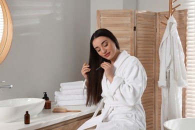 Young woman applying essential oil onto hair in bathroom