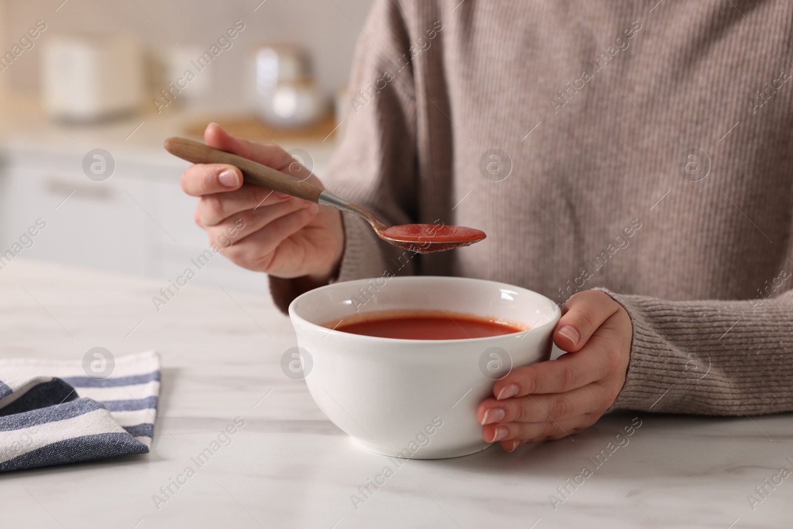 Photo of Woman eating tasty tomato soup at white marble table, closeup