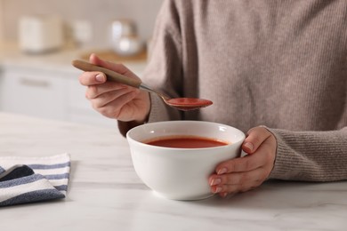 Woman eating tasty tomato soup at white marble table, closeup