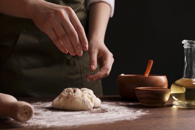Photo of Woman adding spices onto dough at wooden table, closeup. Cooking traditional grissini