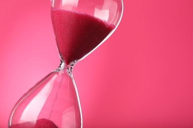 Photo of Hourglass with flowing sand on pink background. Space for text