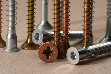 Photo of Many metal screws on beige background, closeup