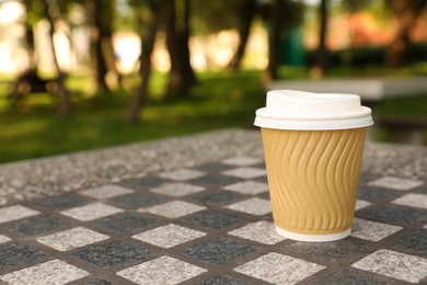 Photo of Paper cup on table in park, space for text. Coffee to go