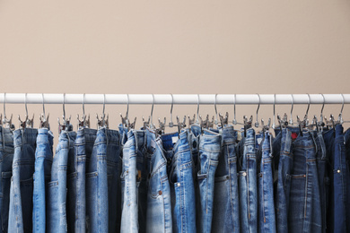 Photo of Rack with stylish jeans on beige background, closeup