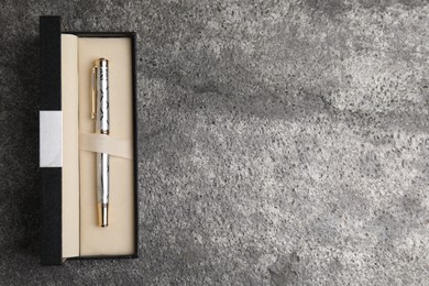 Photo of Beautiful ornate fountain pen in box on grey table, top view. Space for text