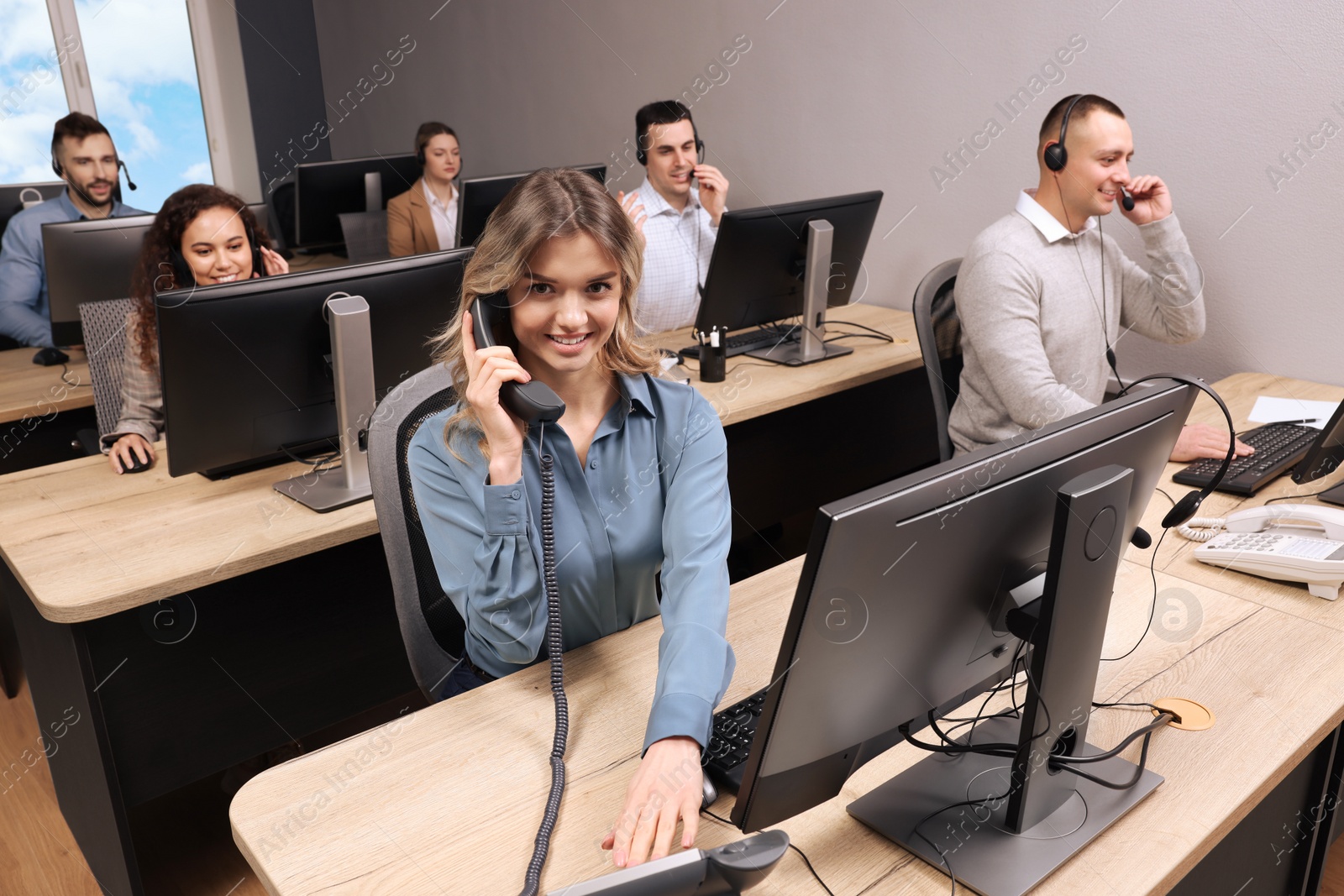 Photo of Young call center operator talking on phone and her colleagues working in modern office