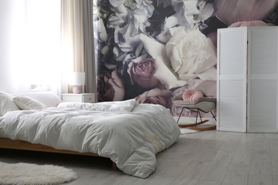 Photo of Comfortable bed near wall with floral wallpaper. Stylish room interior