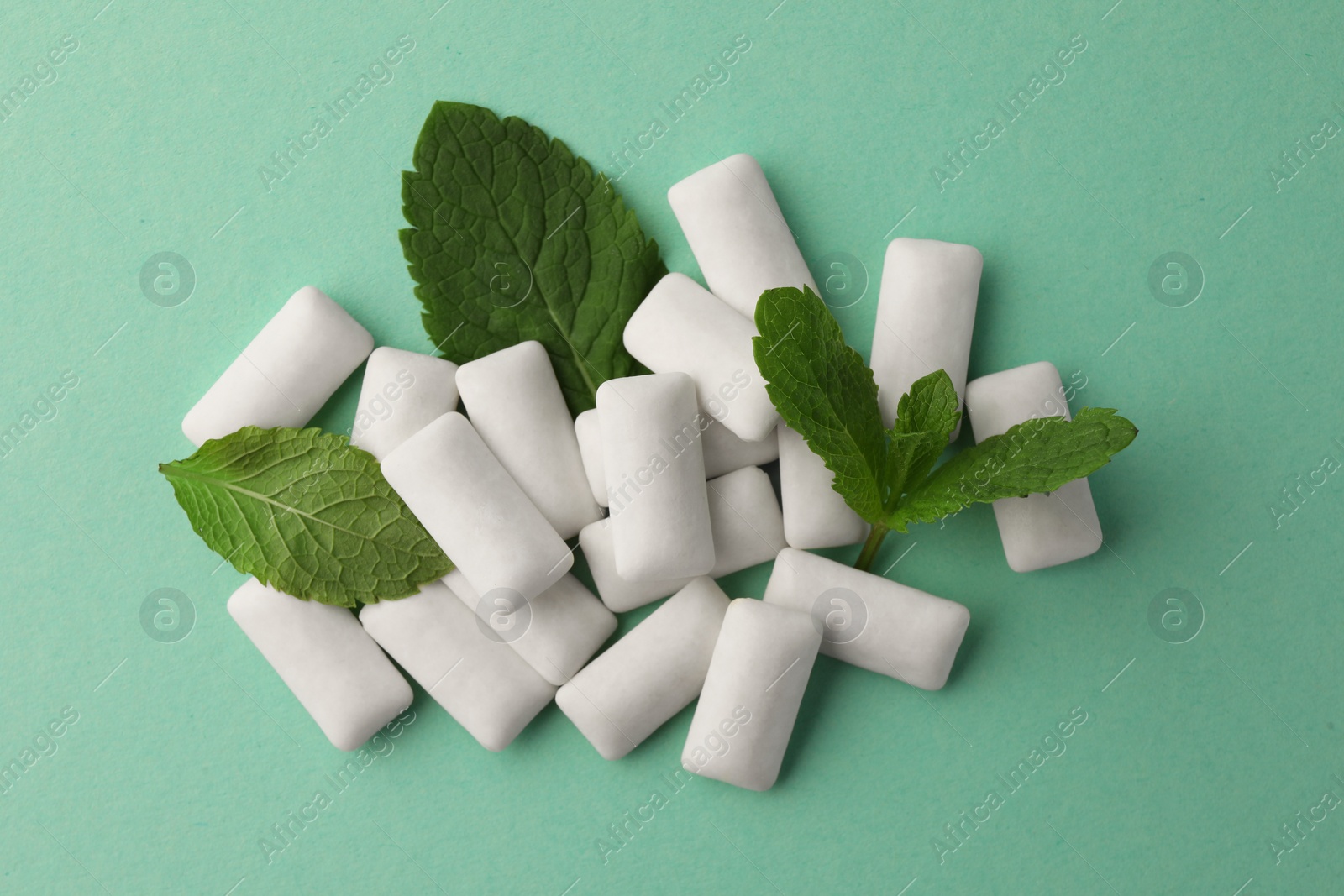 Photo of Tasty white chewing gums and mint leaves on turquoise background, top view