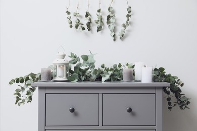 Photo of Stylish chest of drawers decorated with beautiful eucalyptus garland and candles indoors