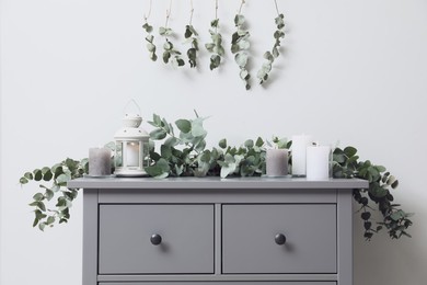 Stylish chest of drawers decorated with beautiful eucalyptus garland and candles indoors