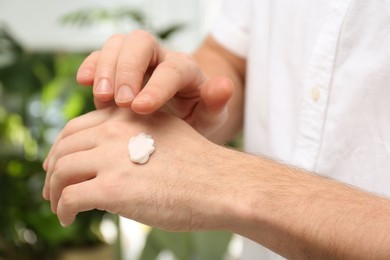 Photo of Man applying moisturizing cream onto hand on blurred background, closeup