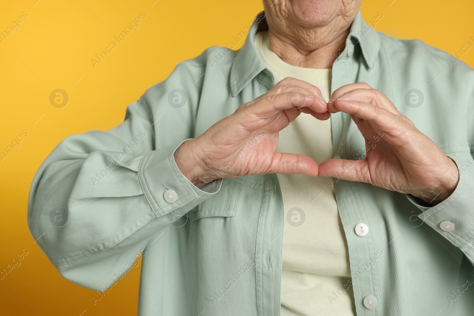 Photo of Elderly woman making heart with her hands on yellow background, closeup