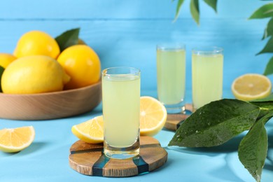 Photo of Tasty limoncello liqueur, lemons and green leaves on light blue table