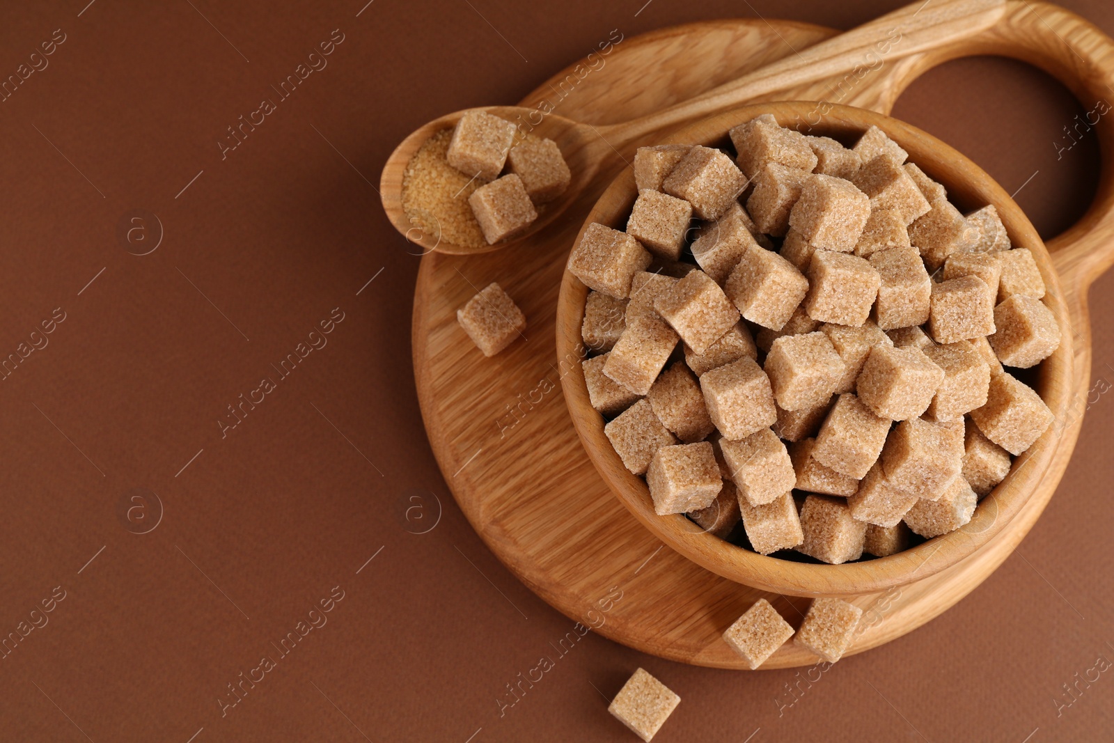 Photo of Brown sugar cubes in bowl and spoon on color background, top view. Space for text