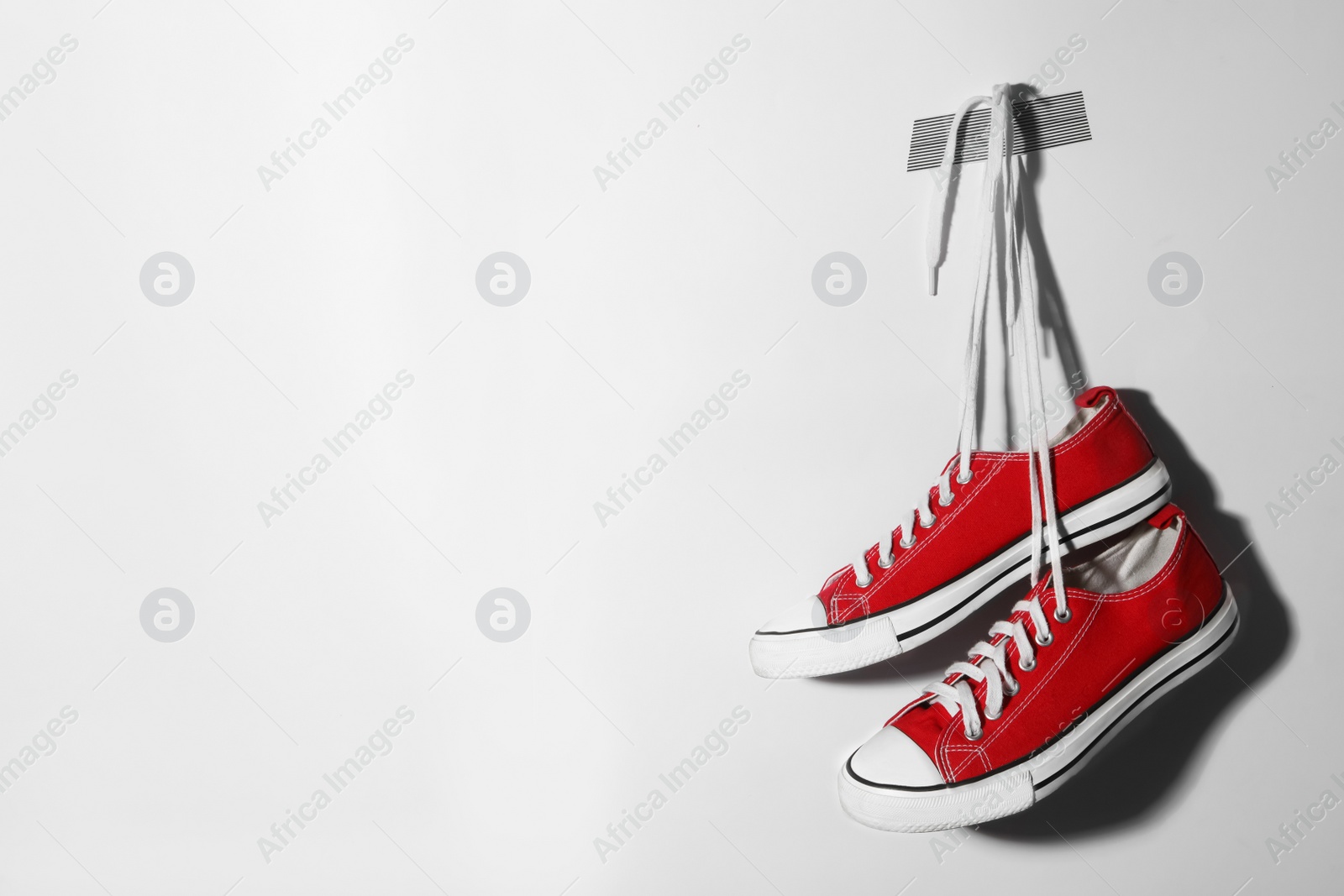 Photo of Pair of stylish shoes with laces hanging on white wall, space for text
