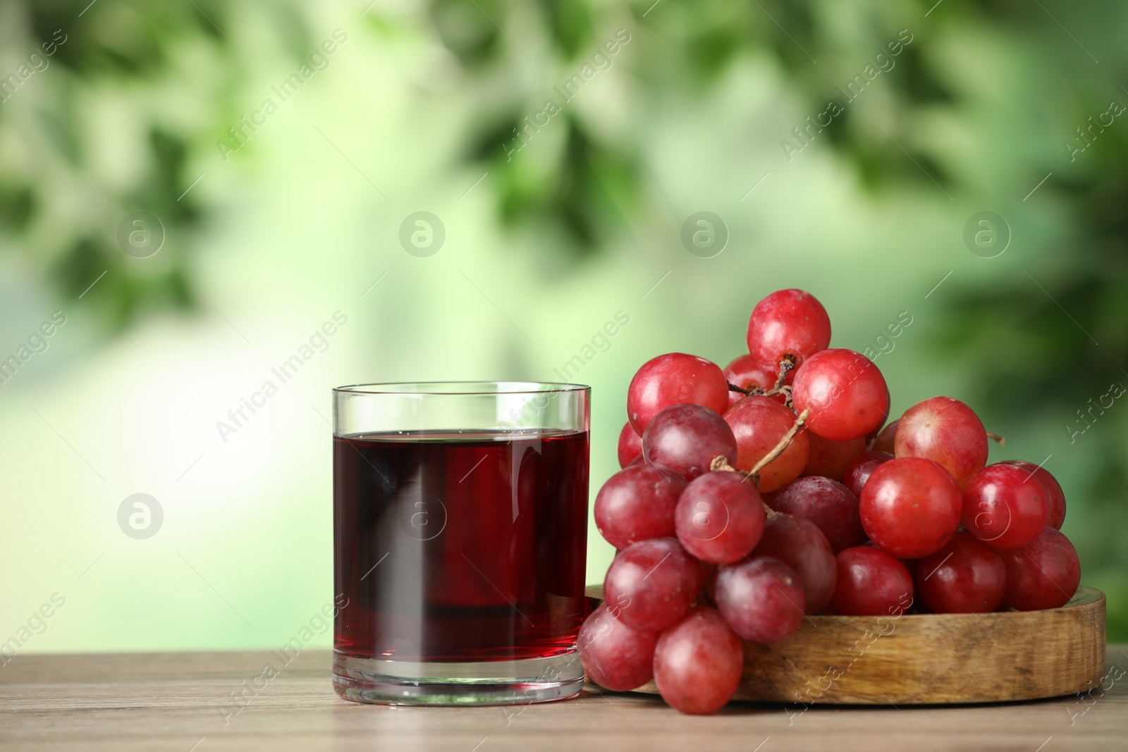 Photo of Glass of juice and fresh grapes on wooden table outdoors