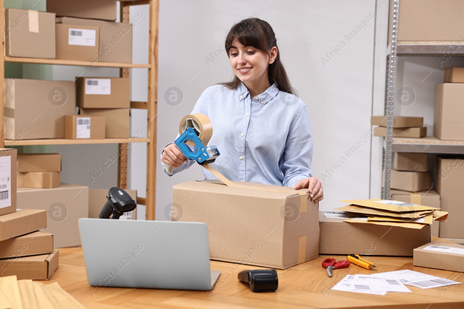 Photo of Parcel packing. Post office worker taping box at wooden table indoors