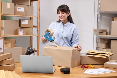 Photo of Parcel packing. Post office worker taping box at wooden table indoors