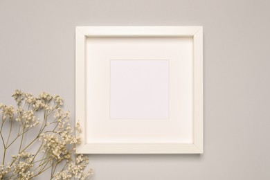 Photo of Empty photo frame and beautiful gypsophila flowers on light gray background, flat lay. Mockup for design