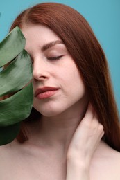 Beautiful woman with freckles and monstera leaf on light blue background