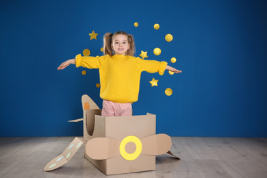 Cute little child playing with cardboard plane near blue wall