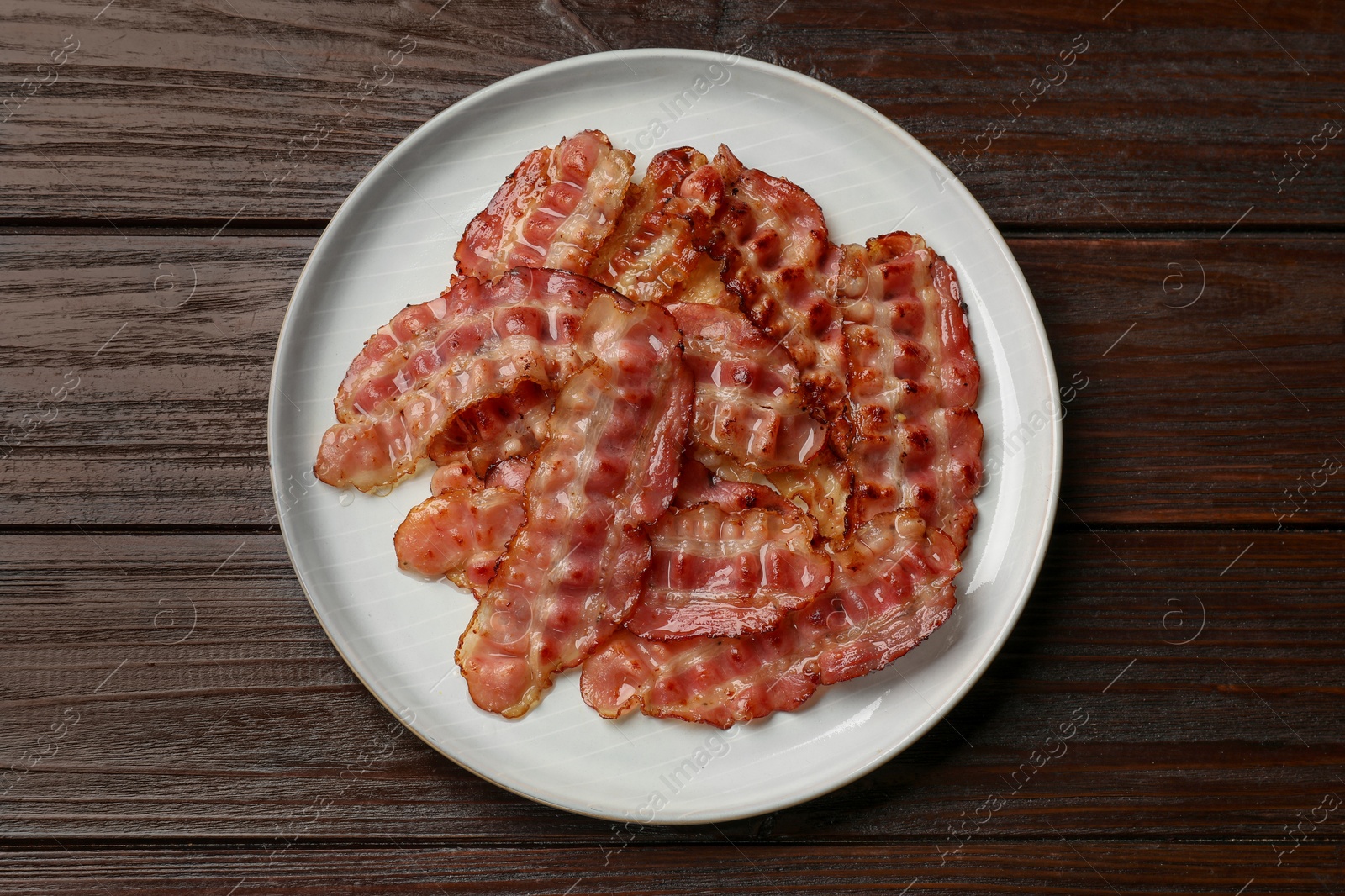 Photo of Plate with fried bacon slices on wooden table, top view