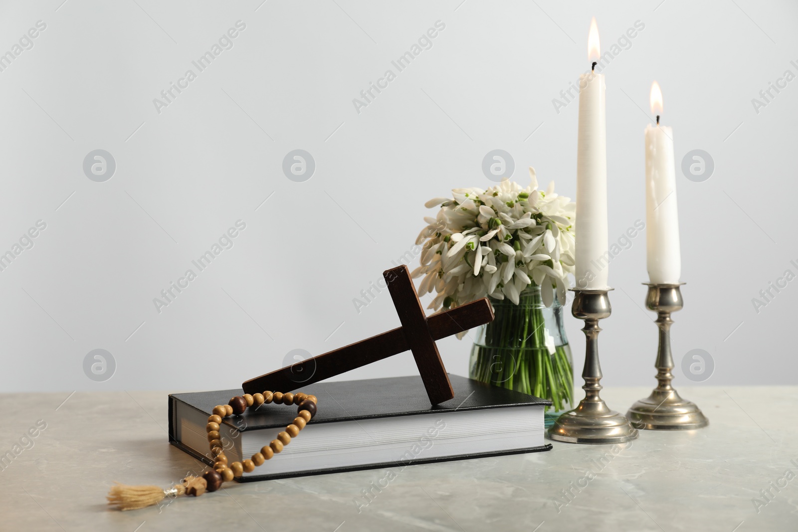 Photo of Wooden cross, rosary beads, Bible, church candles and flowers on marble table. Space for text