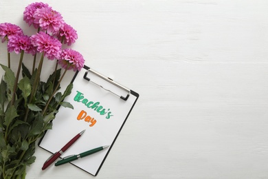 Photo of Beautiful flowers and clipboard with words TEACHER'S DAY on white wooden background, flat lay. Space for text