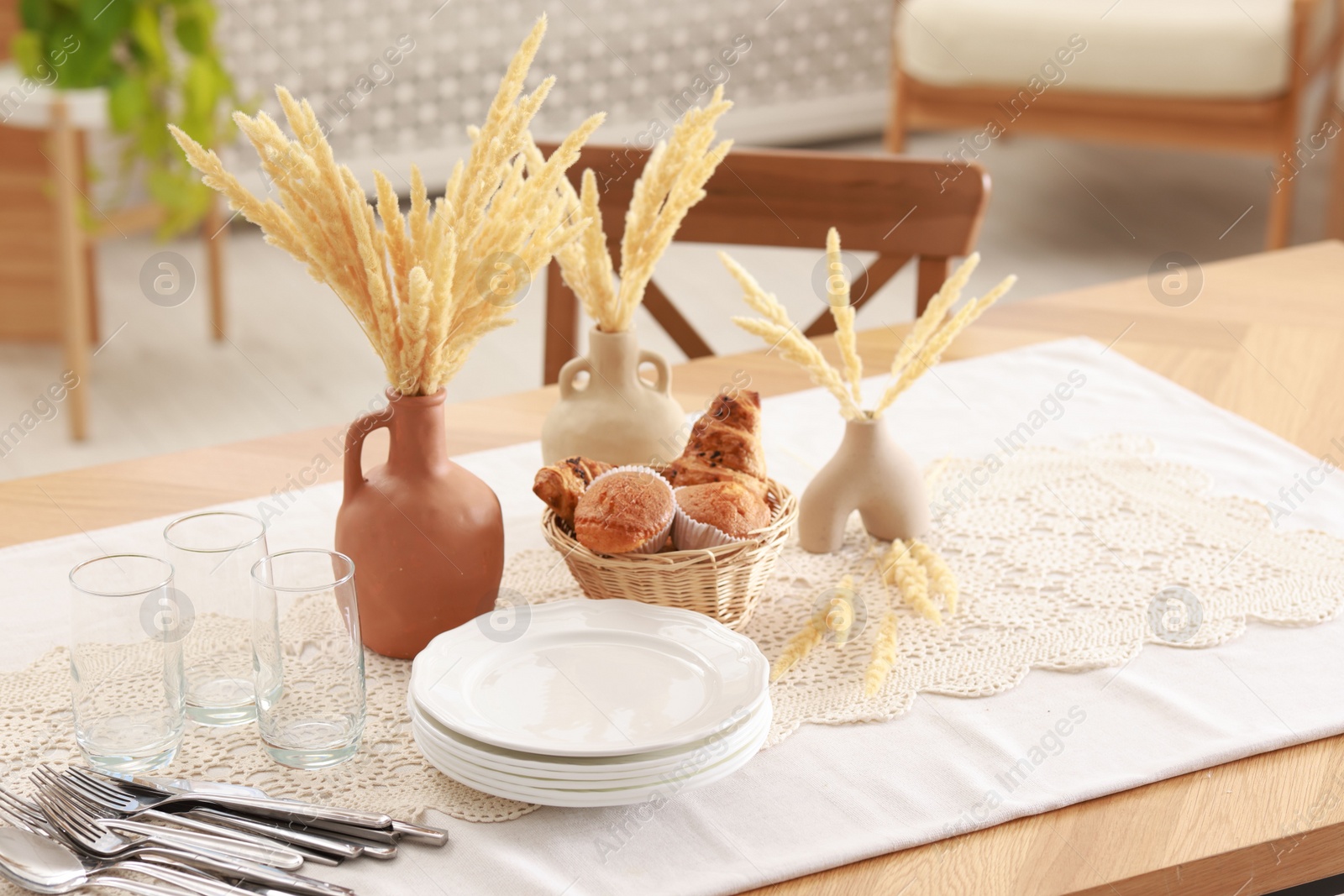 Photo of Clean dishes, dry spikes and fresh pastries on table in stylish dining room