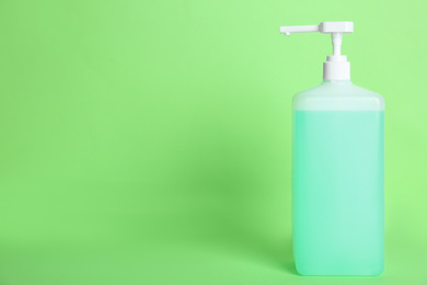 Photo of Dispenser bottle with antiseptic gel on green background. Space for text