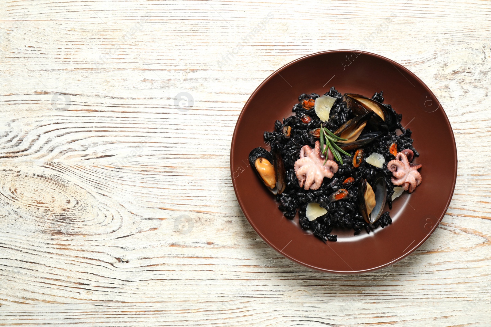 Photo of Delicious black risotto with seafood on white wooden table, top view. Space for text