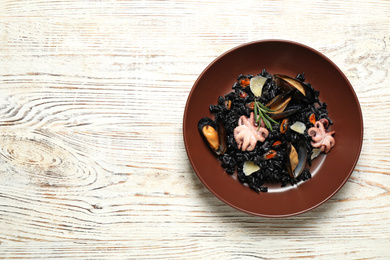 Delicious black risotto with seafood on white wooden table, top view. Space for text