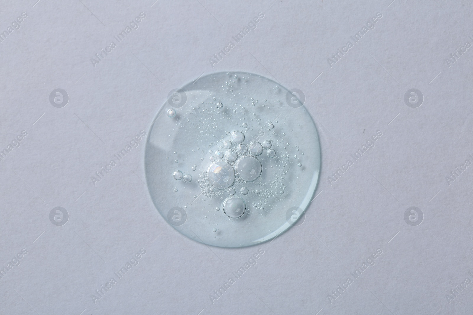 Photo of Drop of cosmetic serum on white background, top view