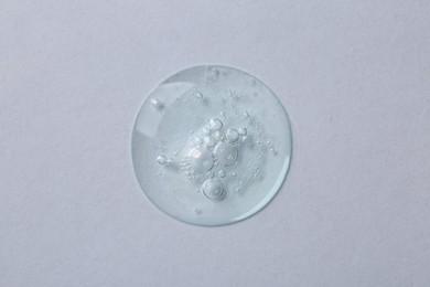 Photo of Drop of cosmetic serum on white background, top view