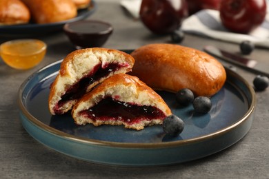 Photo of Delicious baked patties with jam and blueberries on grey table, closeup