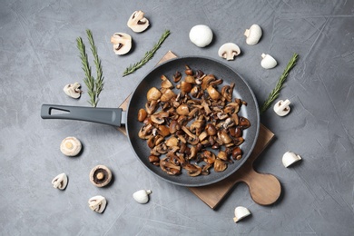 Frying pan with mushrooms on grey background, flat lay