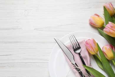 Photo of Stylish table setting with cutlery and tulips on white wooden background, flat lay. Space for text