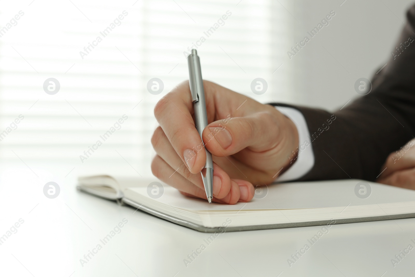 Photo of Man writing in notebook at white table indoors, closeup