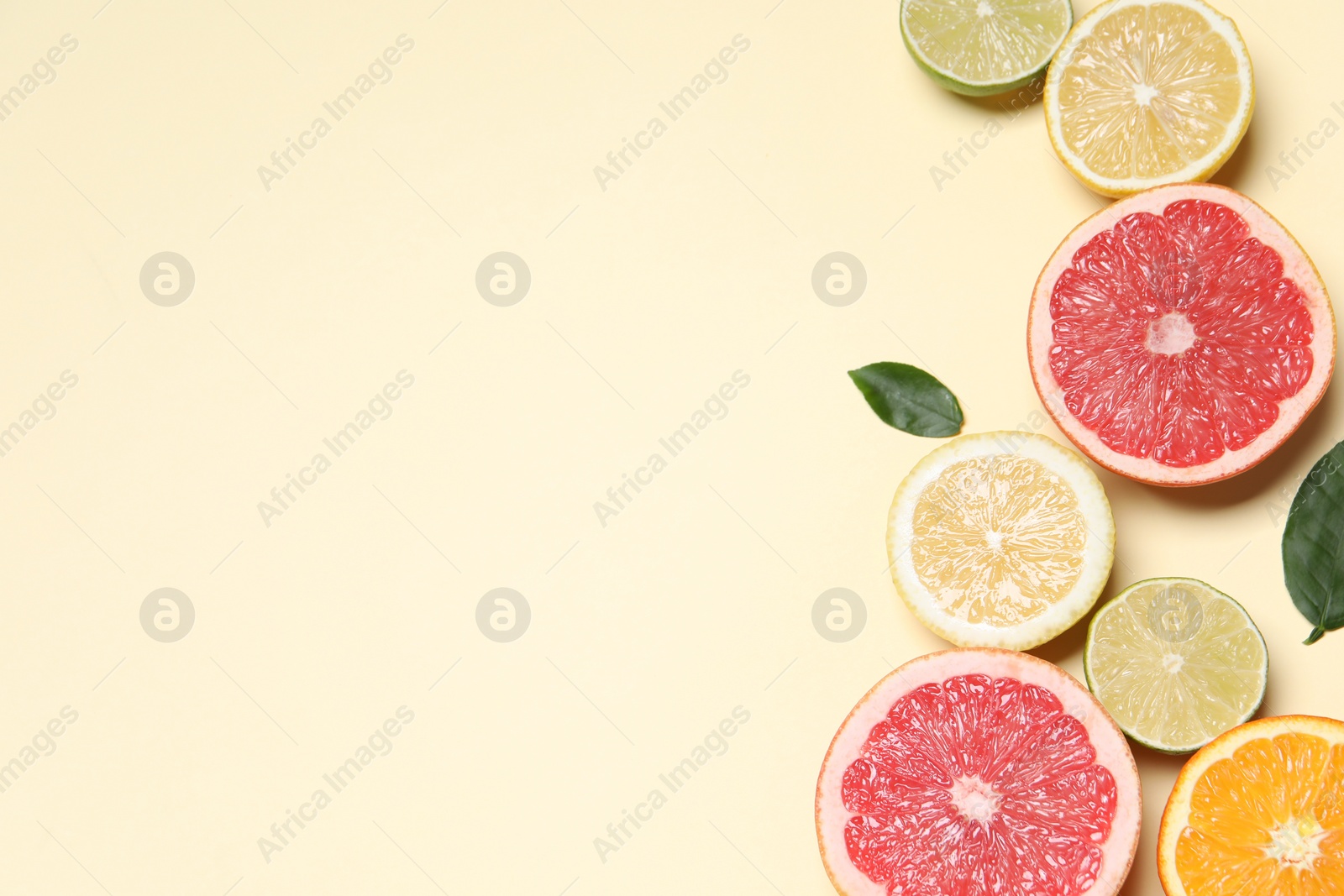 Photo of Different cut citrus fruits and leaves on beige table, flat lay. Space for text