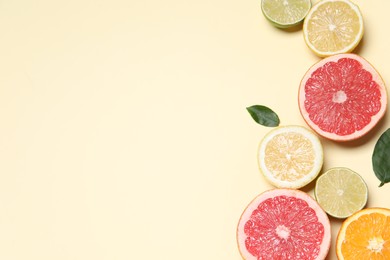 Different cut citrus fruits and leaves on beige table, flat lay. Space for text