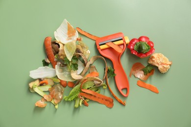 Photo of Peels of fresh vegetables and peeler on green background, flat lay