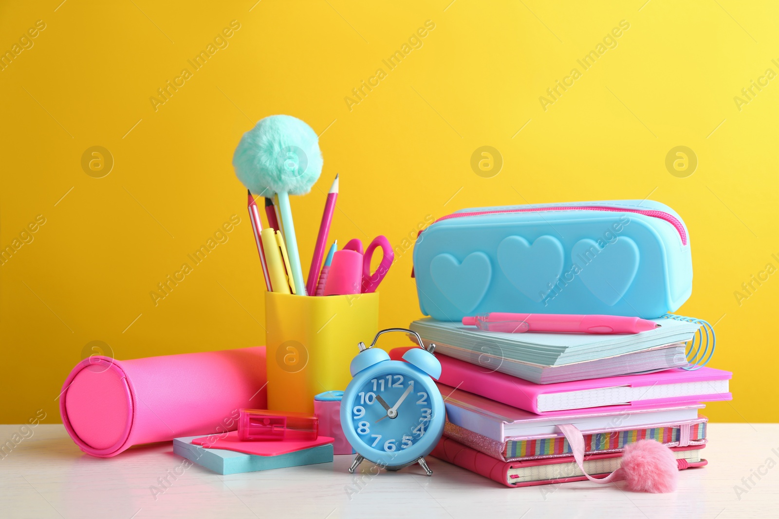 Photo of Different school stationery on white wooden table against yellow background