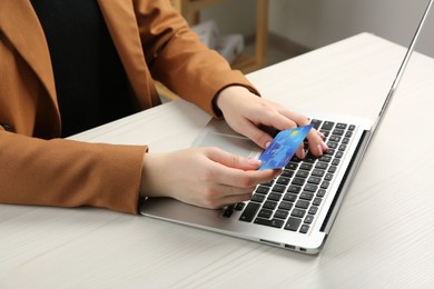 Online payment. Woman with credit card using laptop at white wooden table indoors, closeup