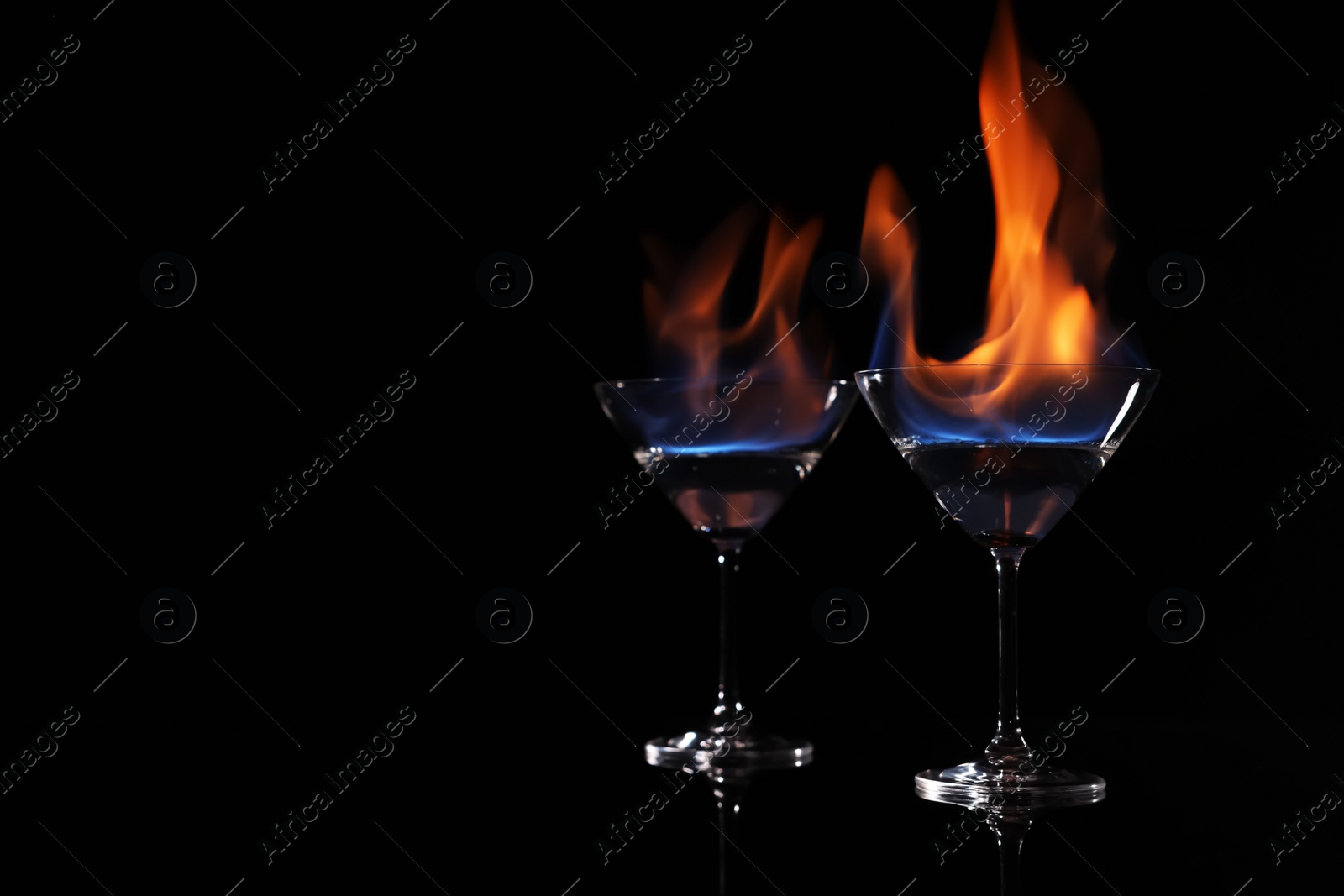 Photo of Cocktail glasses with flaming vodka on black background, space for text